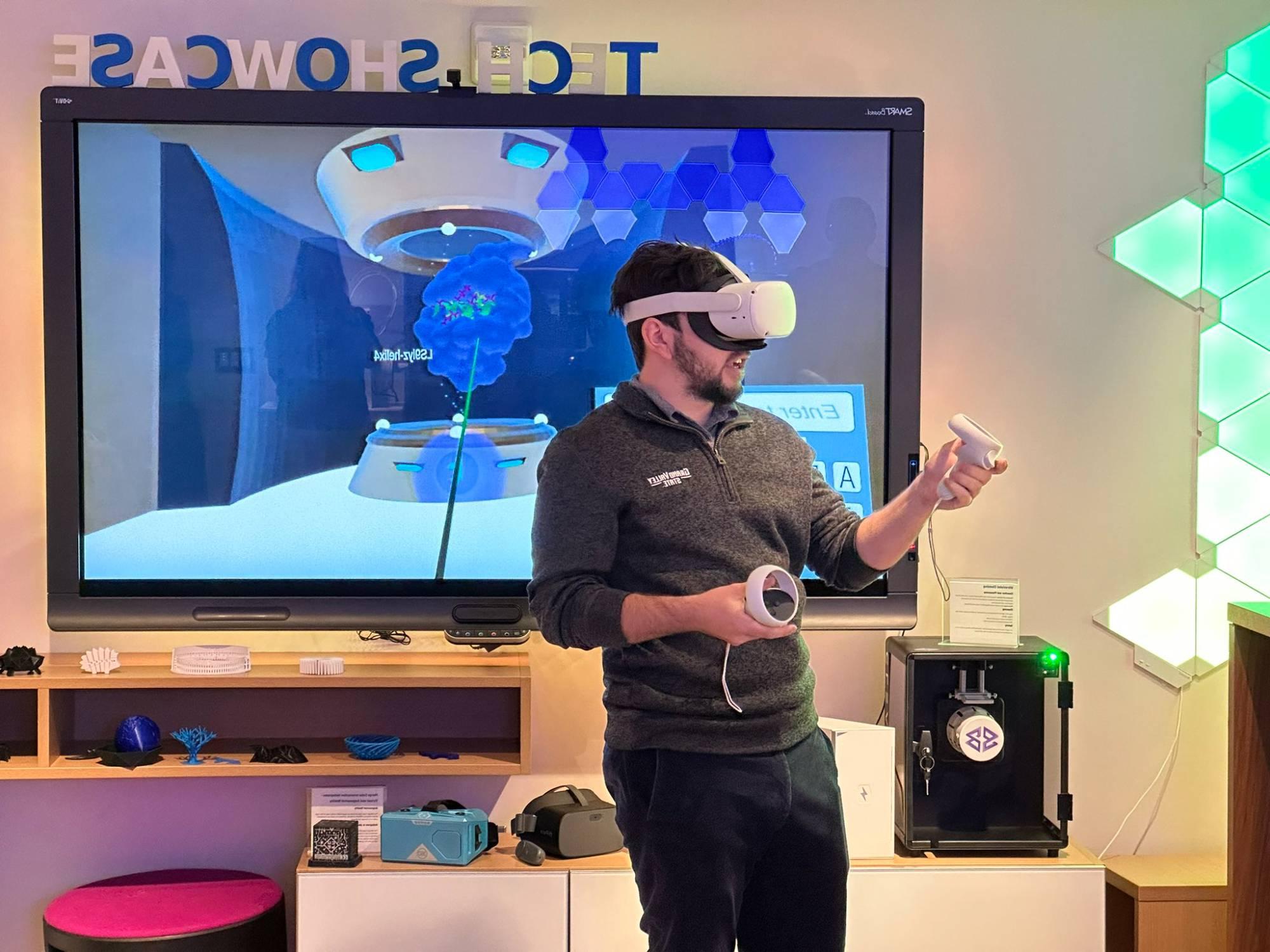 Man in grey shirt and jeans wearing virtual reality headset with large tv screen in the background